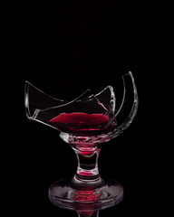 An unusual photo of cracked wine glass with few wine inside isolated on black background.