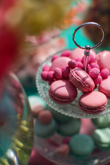 Candy bar with macaroons on a stand. Decorative sweet wedding table in bright colors of blue, turquoise and pink. Decorated with lanterns, pillows, upholstered furniture, watches and flowers.