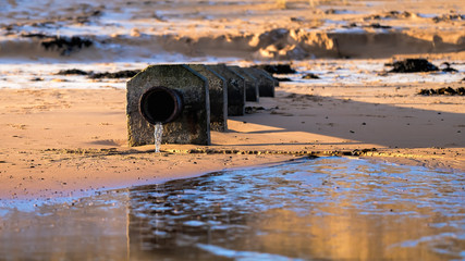 Effluent pipe discharging onto a beach in golden winter light with light snow patches on the sand