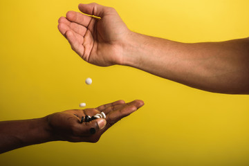 Fototapeta premium two male hands one black male second European man holding and flipping pills white and black