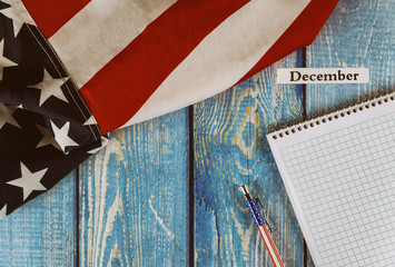 December month of calendar year United States of America flag of symbol of freedom and democracy with blank notepad and pen on office wooden table