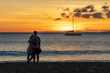 Embraced couple watching the beautiful Hawaiian sunset on a sandy beach on Maui.