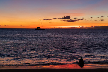 Naklejka na ściany i meble Little boy sitting in the warm Hawaiian ocean, watching the beatiful sunset.