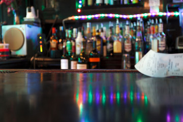 Defocused bar scene . Reflection on bars with bar tab. Bottles in background.