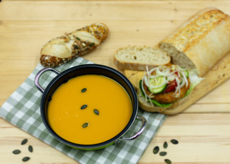 Kürbissuppe im Topf daneben ein Bratling auf Brot mit Tomaten, Zwiebeln und Salat.
