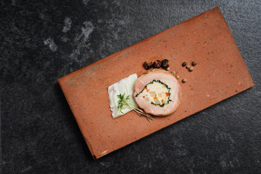 quail galantine, de-boned stuffed meat as a festive appetizer served on a brick on dark slate with copy space