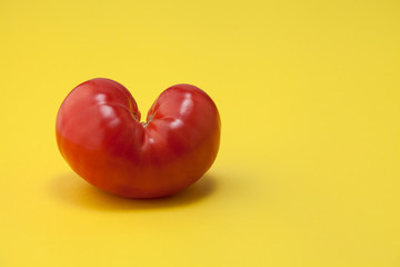 Photo of one ripe tomato on a yellow background.