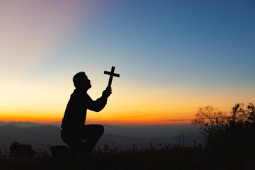 Human praying and holding christian cross for worshipping God at sunset sky background.Christian, Christianity, Religion copy space background.