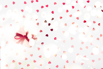 Craft box with red ribbon bow and glitter heart confetti. Valentine day and eco-friendly wrapping concept. Trendy minimalistic flat lay design background. Horizontal with festive bokeh lights