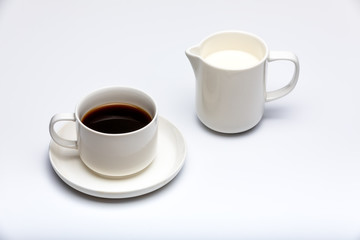 Creamer with milk and cup of coffee on white background