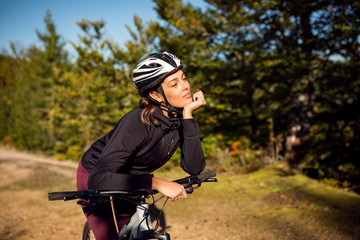 Cute young female cyclist with bike in nature environment