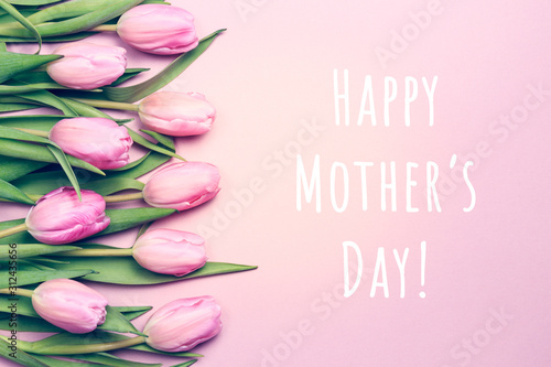 Happy Mother's day wording with pink tulips on the pink background. Flat lay, top view. Mother's day holiday celebration card. Horizontal, flowers on the left side