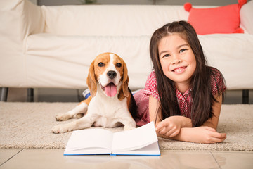 Little Asian girl with cute beagle dog reading book at home