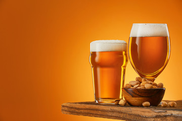 Glasses of beer and snack on table against color background