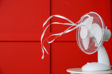 Fototapeta Electric fan with fluttering ribbons near color wall obraz