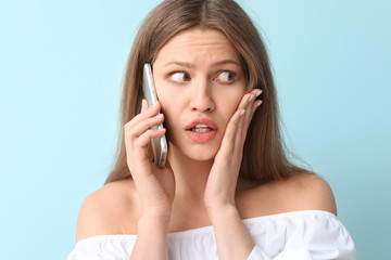 Fototapeta premium Afraid woman talking by mobile phone on color background