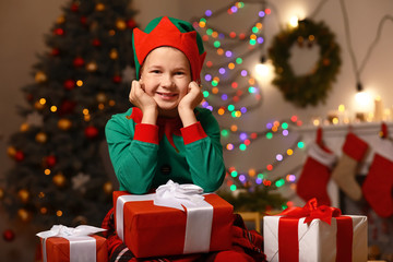 Fototapeta na wymiar Little boy in costume of elf and with gifts in room decorated for Christmas