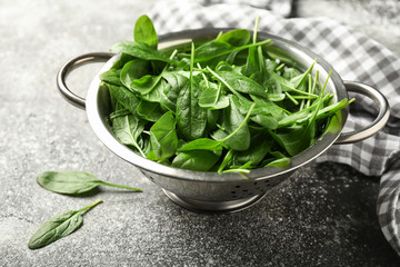 Colander with fresh spinach on table
