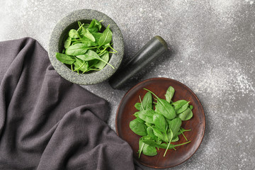 Mortar, pestle and plate with fresh spinach on grey background