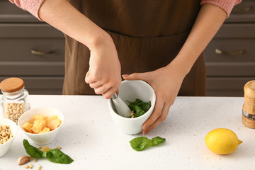 Woman preparing healthy pesto sauce in kitchen