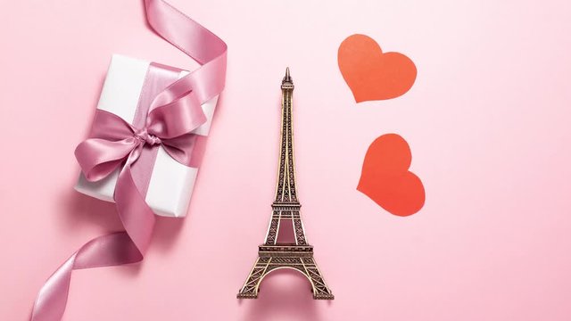 The Eiffel Tower, red hearts and white gift with purple ribbon bow on bright background. Stop motion animation with copy space. Romantic, love and Valentines day concept 