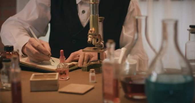 Scene tracks around a Victorian era scientist working in his laboratory using a dip pen to make some notations in a notebook of his work.