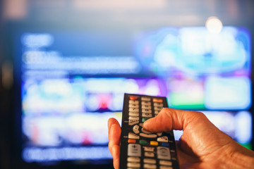 Hand mit Fernbediehnung vor großem TV Bildschirm auswählen / Online Streaming Netflix /...