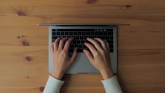 Hands typing on laptop on wooden desk