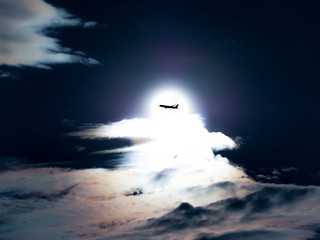 aircraft flying cross the moon in cloudy sky