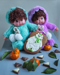 Fototapeta na wymiar Greeting card with twin dolls in bright costumes with glazed gingerbread and tangerines