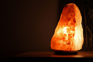 Himalayan salt lamp on wooden table illuminated in a darkend room