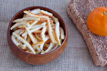 Candied orange peel in wooden bowl with orange on cutting board