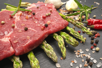 meat food : raw beef fillet on black stone board with asparagus with dry spices ready to cooking