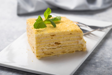 Piece of cake Napoleon on white plate on concrete              background, close up view. Traditional millefeuille dessert with puff pastry and custard, copy space.