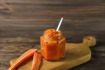 Homemade carrot jam in glass jar on brown wooden background. Healthy sweet sauce