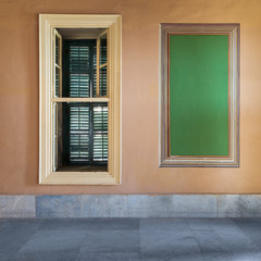 Green frame with ornate border and window with closed green shutter on orange wall with marble floor