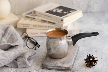 Hot chocolate pot on concrete grey background with candle and books. Hygge style concept.
