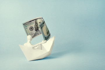 a man of white plasticine sits in a paper boat and holds a bill in his hands like a sail. business concept..