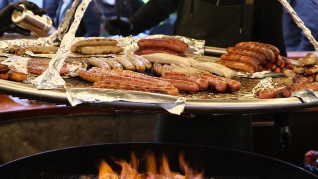 Pork, chiken and beef grilled sausages are fried in a large pan over an open fire. Outdoor cafe prepares a treat for the tourists at the fair.