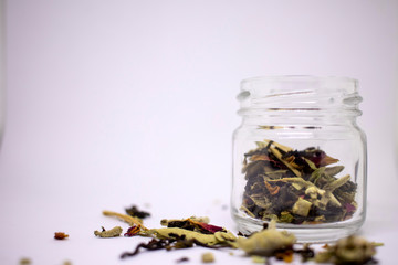 A mixture of bio herbal and flower dried tea. In a jar and in bulk on a white background. Place for text. Close-up.