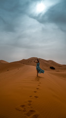 Women in blue and white dress walking on the sand dune in Sahara desert in Morocco
