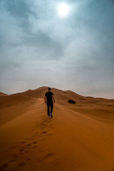 Man in black clothes walking on the sand dune in Sahara desert in Morocco