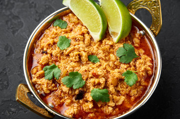 Chicken keema in traditional indian copper kadai at dark slate background. Kheema is indian and pakistani cuisine curry dish with minced meat and spices. Close up