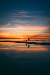 Little girl in a hat with women on the sea shore in Baltics with a red and orange sky at the sunset