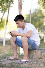 A man is sitting on the street playing a game on his mobile phone