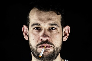 Male face and a burning cigarette in his mouth.Male face and burning cigarette in his mouth.Man in front of black background.