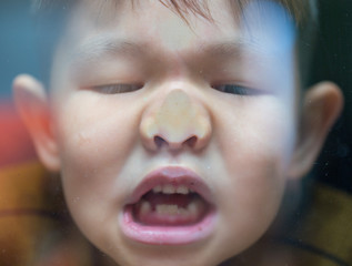 Curious child standing behind the glass and pressing his nose on a glass window