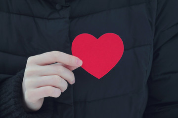 Girl holding a cardboard heart in front of her heart on black background. Stock photography for st. valentine's day.