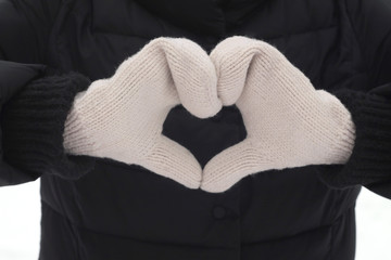 Girl in white mittens and winter clothes makes heart with hands on black background. Stock photography for st. valentine's day.