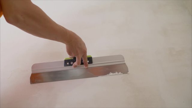 a close shot at the builder hands, who level the wall with a long spatula and plaster, the man applies the composition on the surface. Worker aligns the wall with a spatula. Worker aligns the wall wit